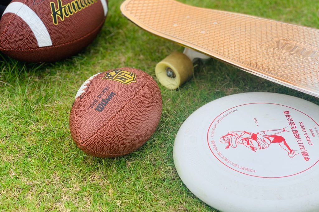 A close-up of sports equipment including a football, skateboard, and frisbee on grass.