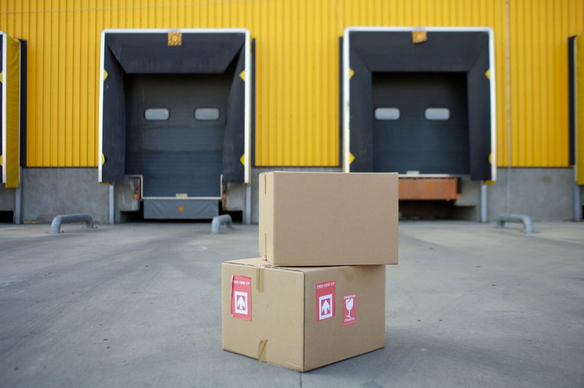 Cardboard boxes stacked in front of industrial warehouse loading docks with yellow walls.