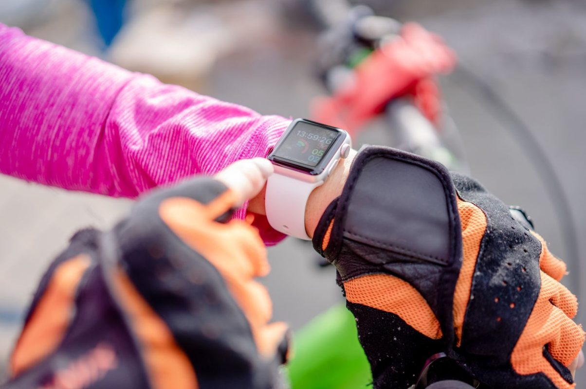 Close-up of a cyclist wearing gloves checking a smartwatch outdoors.