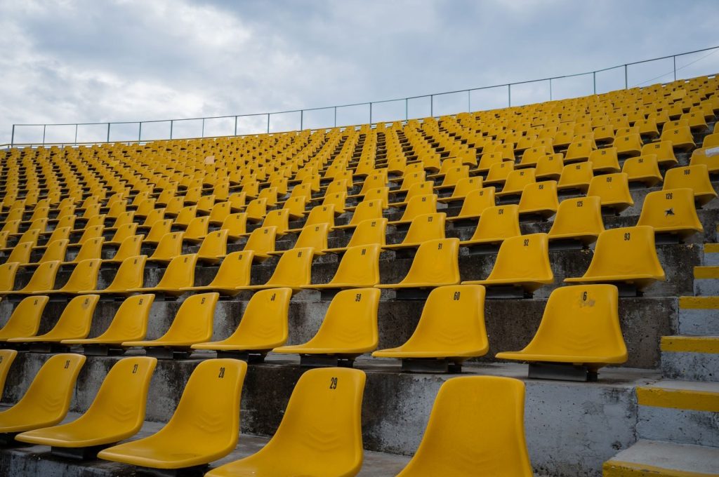 View of empty yellow seats arranged in rows at a stadium on a cloudy day.