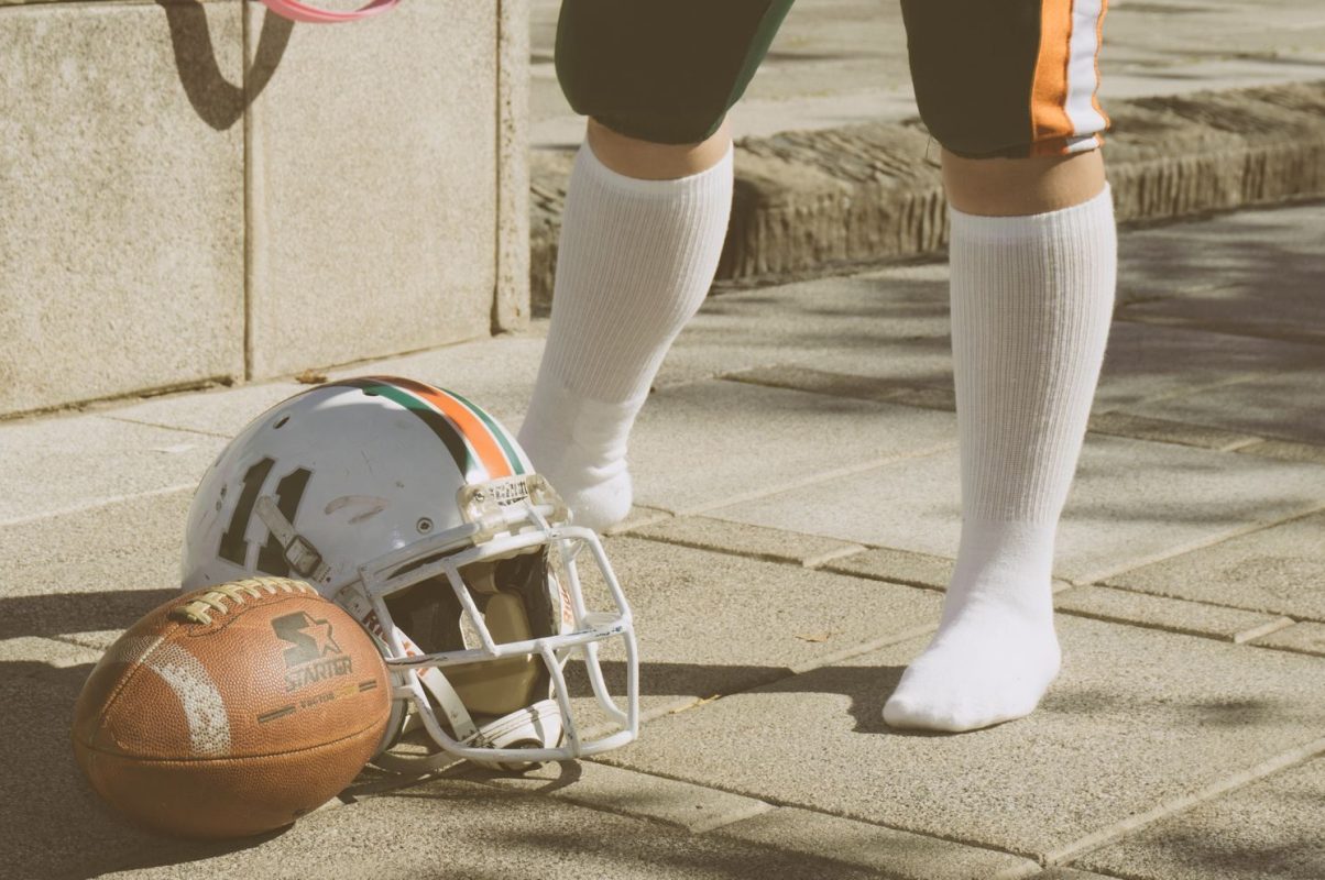 American football gear including helmet and ball on a city pavement, with player in background.