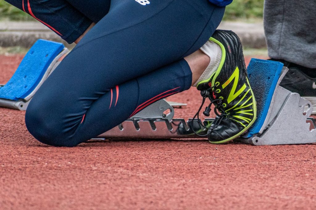 Close-up of a runner's legs ready to start a race, showcasing running shoes and starting block.