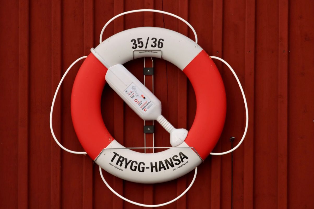 A lifebuoy with rope for emergencies mounted on a red wall, featuring Trygg-Hansa branding.