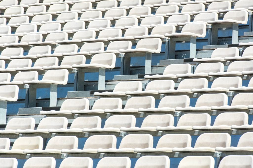 Rows of empty white plastic seats in a stadium, lined up under bright sunlight.