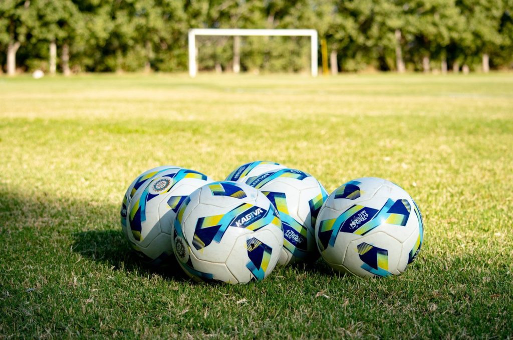 Five soccer balls rest on a green field, ready for a game in Mendoza, Argentina.