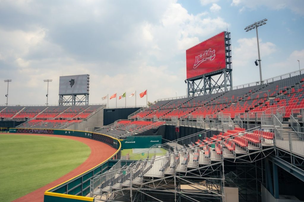 Wide-angle view of empty baseball stadium with red seats and clear sky.