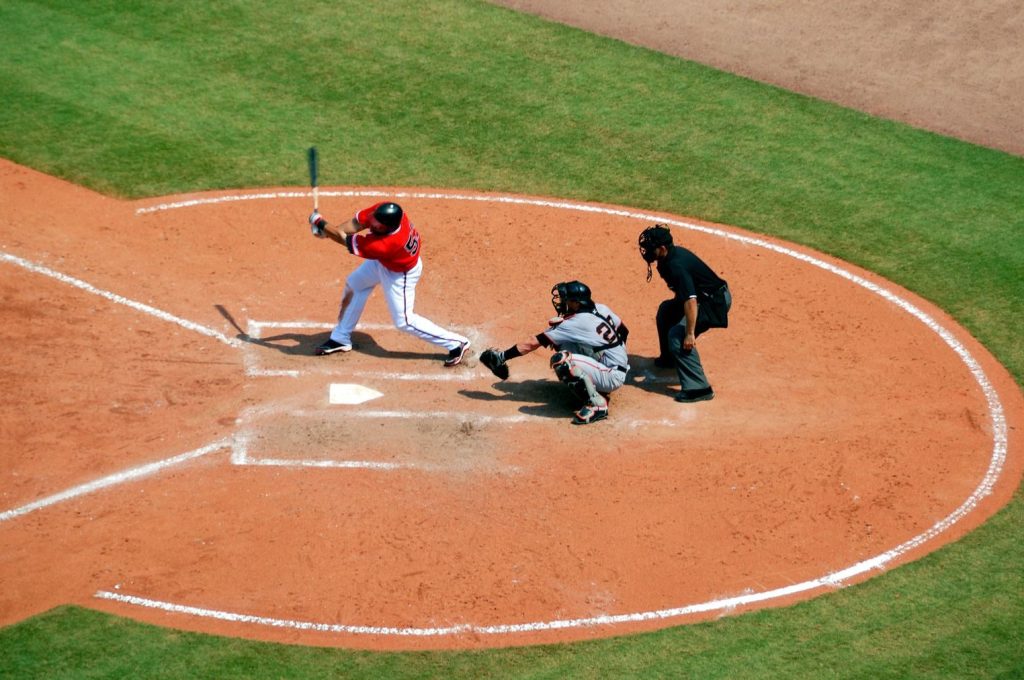 Action shot of a baseball game with batter swinging, catcher, and umpire observing play.