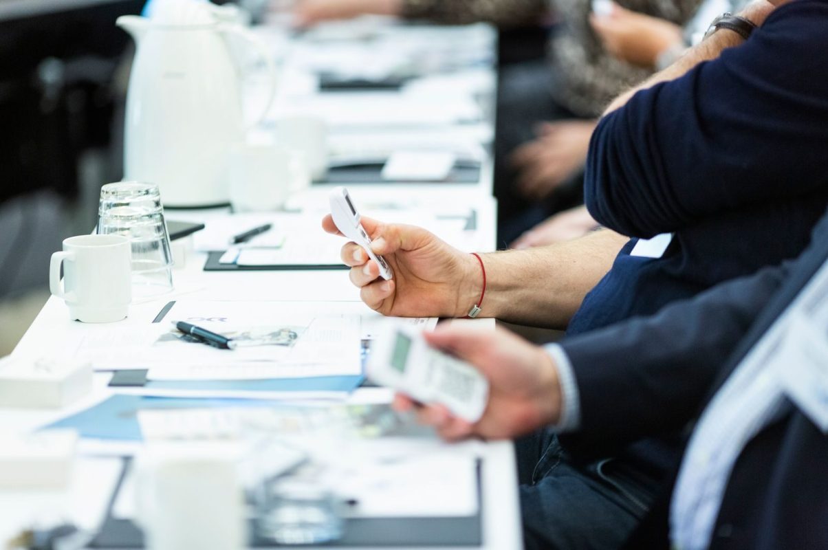Close-up of hands holding devices during a business meeting, highlighting technology and note-taking.