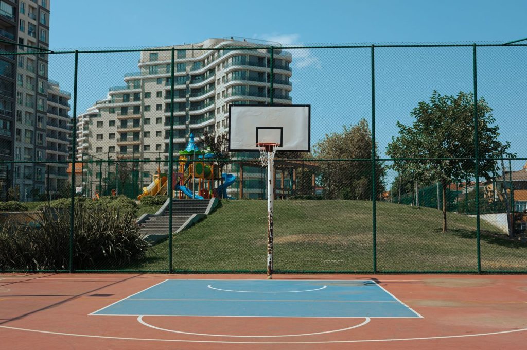 An outdoor basketball court with a hoop and playground in downtown.