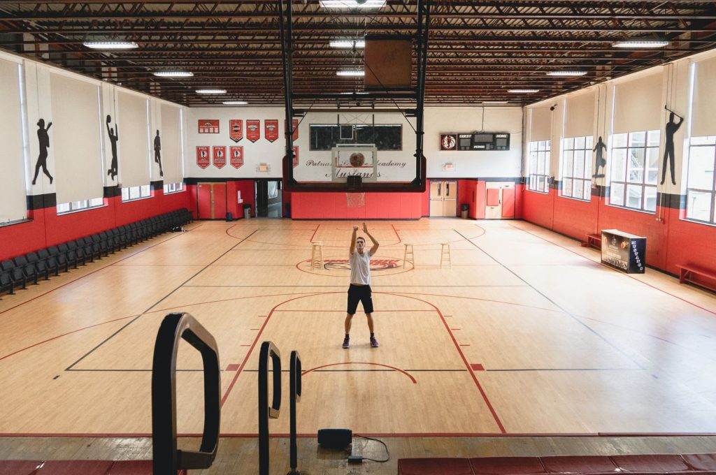 Athlete practicing basketball shots in a spacious indoor gym with wooden flooring.