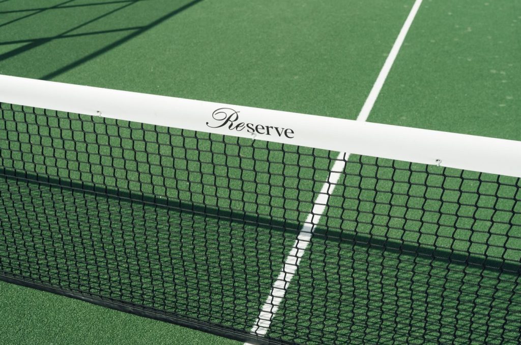 Close-up of a tennis court net displaying 'Reserve' text. Bright green surface.