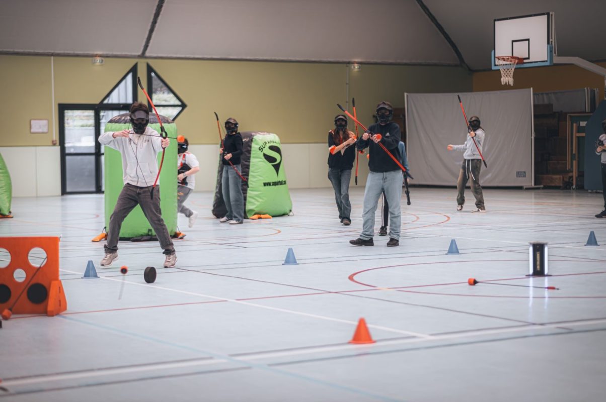 Group playing archery tag indoors with bows, arrows, and masks.