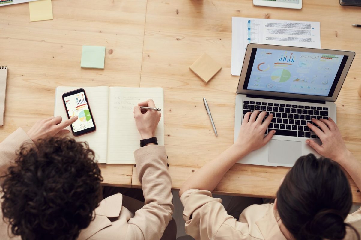 Overhead shot of two colleagues collaborating with devices and notes in a business meeting.