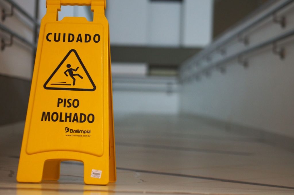 Yellow caution wet floor sign with Portuguese text in an indoor hallway.