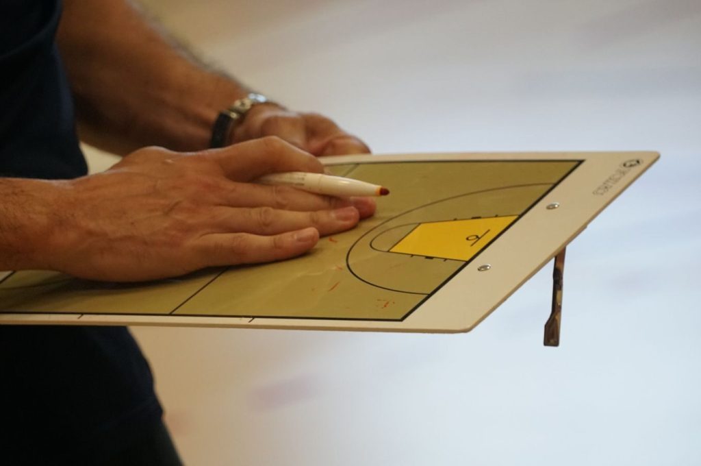 Close-up of a coach using a basketball tactics board to plan game strategy indoors.