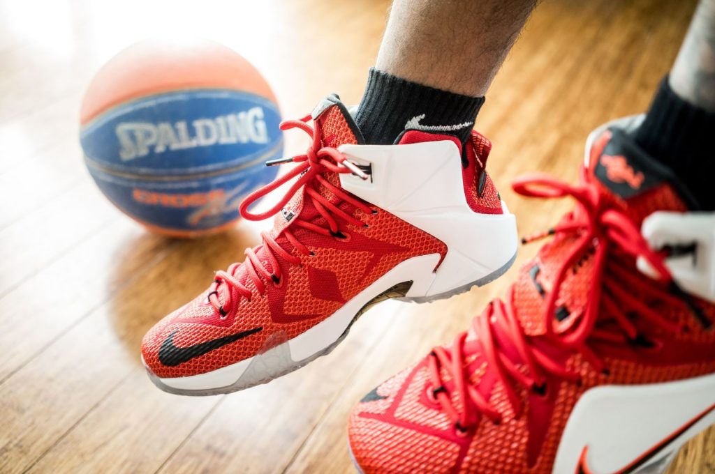 Close-up of red basketball sneakers in action with a Spalding ball on wooden floor.