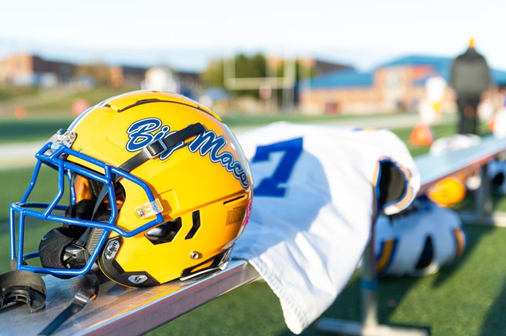 A yellow football helmet with blue highlights rests on a sports bench, ready for the game.