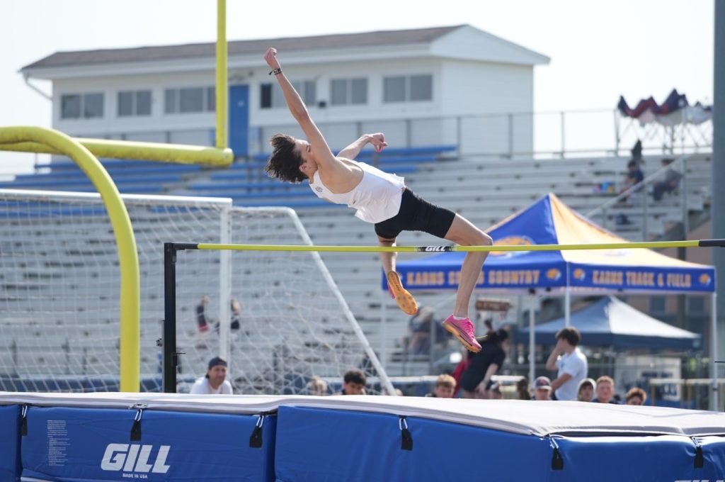 A male high school athlete executing a high jump during a track and field event, outdoors.