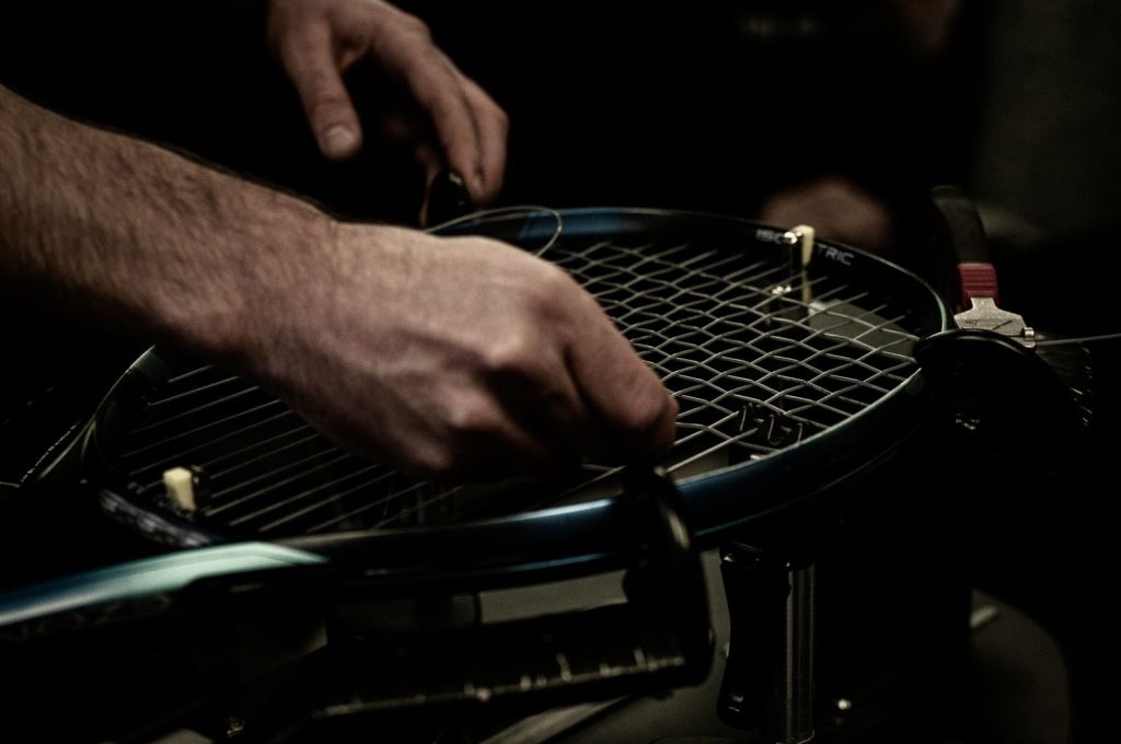 Close-up shot focused on precise stringing of a tennis racket, showing detailed craftsmanship.