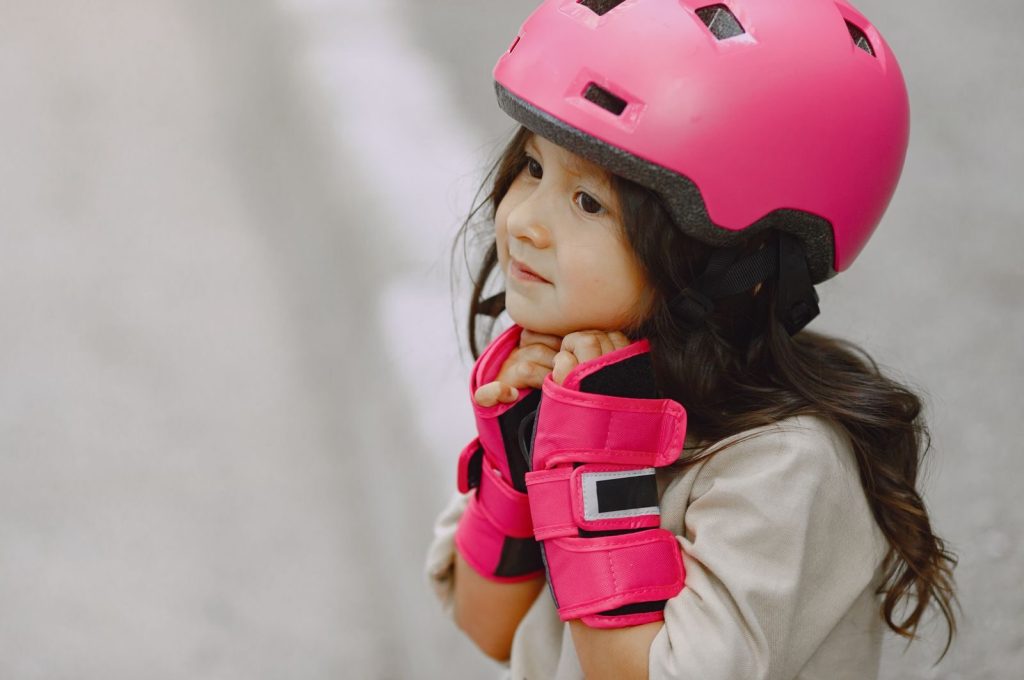 Young girl wearing a bright pink helmet and gloves, providing a side view with a blurred background.