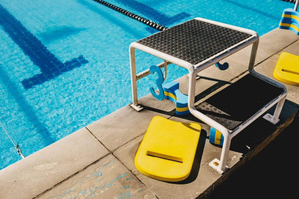 From above of springboard with step and number near swimming boards on poolside in sunlight