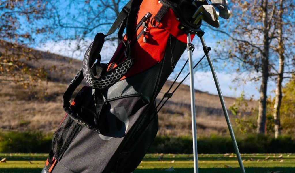 A well-organized golf bag with clubs on a grassy golf course under clear blue skies.