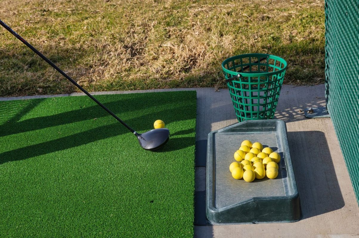 Golf driving range mat with club and yellow balls ready for practice.