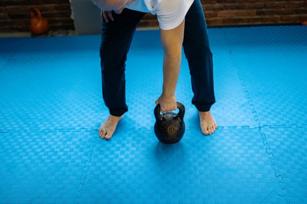 An adult man lifting a kettlebell on blue rubber mats indoors, emphasizing fitness and strength.