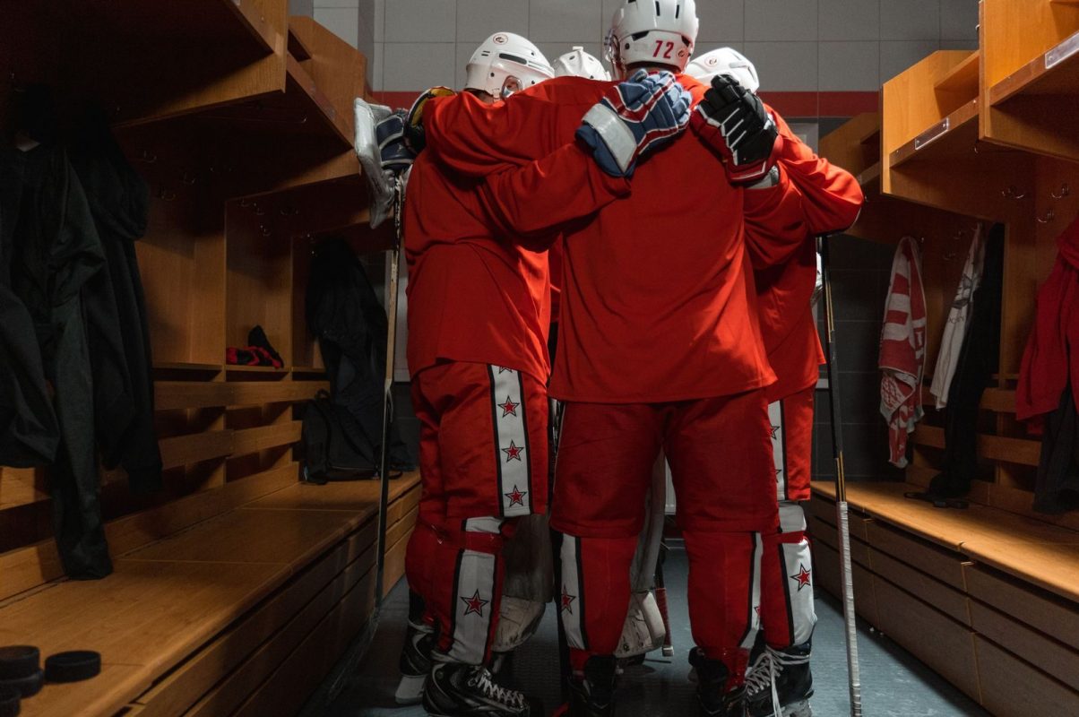 Hockey players in red uniforms huddling in a locker room for motivation and team spirit.