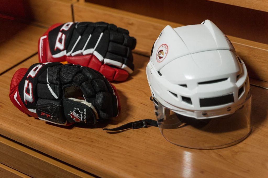 Close-up of hockey gear including helmet and gloves on a wooden bench.