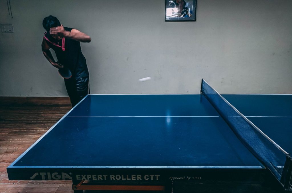 Dynamic action shot of a man playing table tennis indoors, capturing a moment of intense focus and skill.