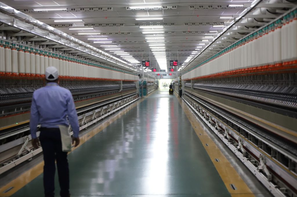Long hallway in a textile factory with a worker walking, showcasing industrial machinery.