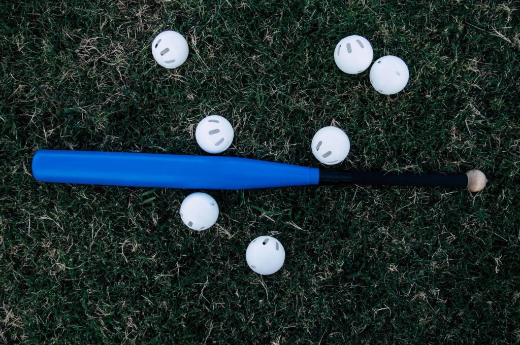 A blue baseball bat surrounded by white practice balls lying on green grass outdoors.