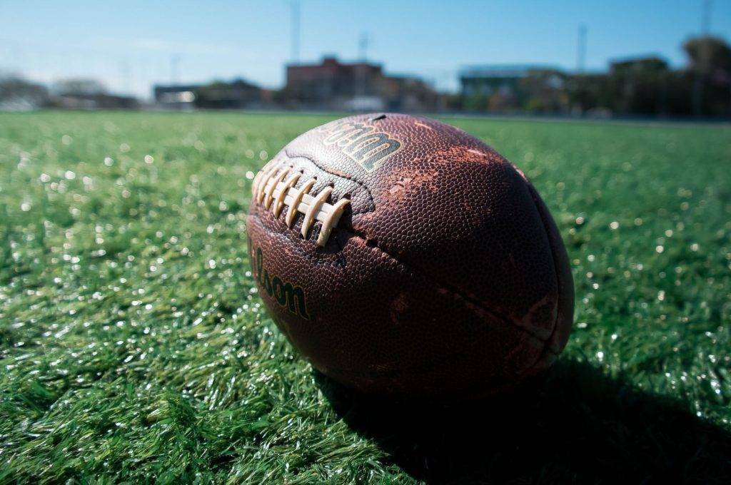 A classic football rests on green grass under blue skies, symbolizing outdoor sports.