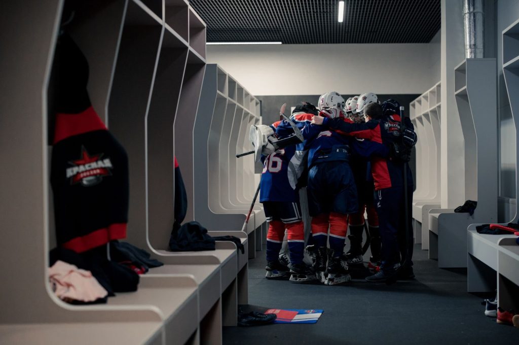 A hockey team in a locker room huddles for motivation, symbolizing teamwork and sportsmanship.