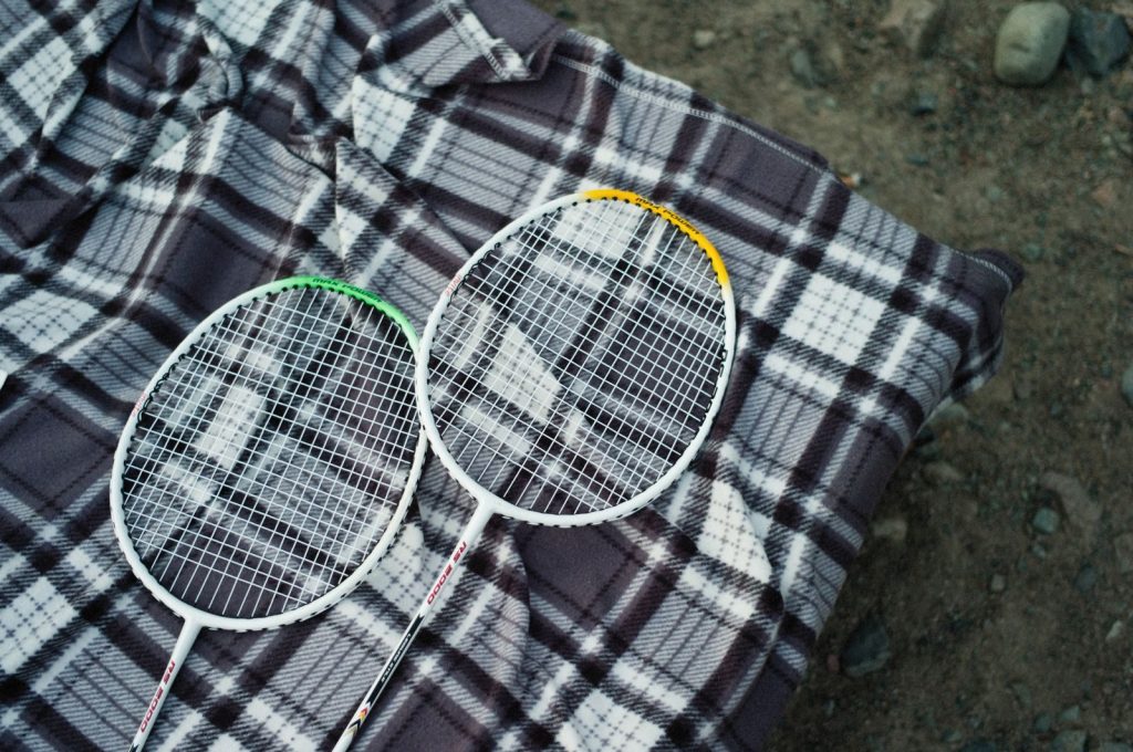 Two badminton rackets resting on a checkered picnic blanket outdoors, ideal for sports and leisure themes.