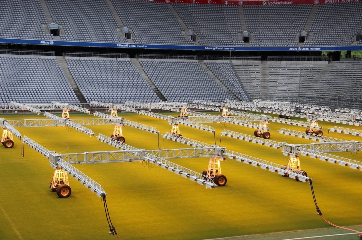 A modern stadium with artificial lighting rigs arranged on a football pitch, creating a unique visual.